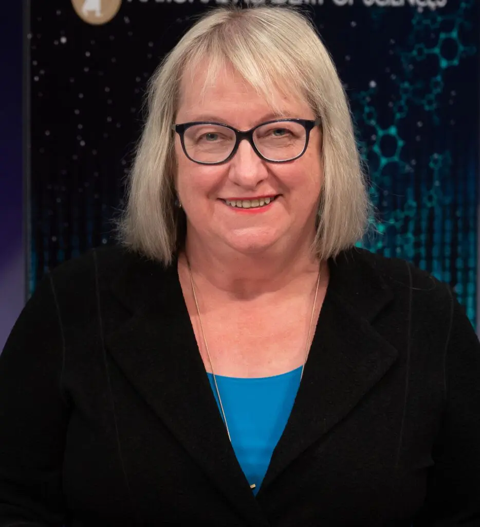 Diana Liverman smiling at the camera with a short blond bob, glasses and a blue top